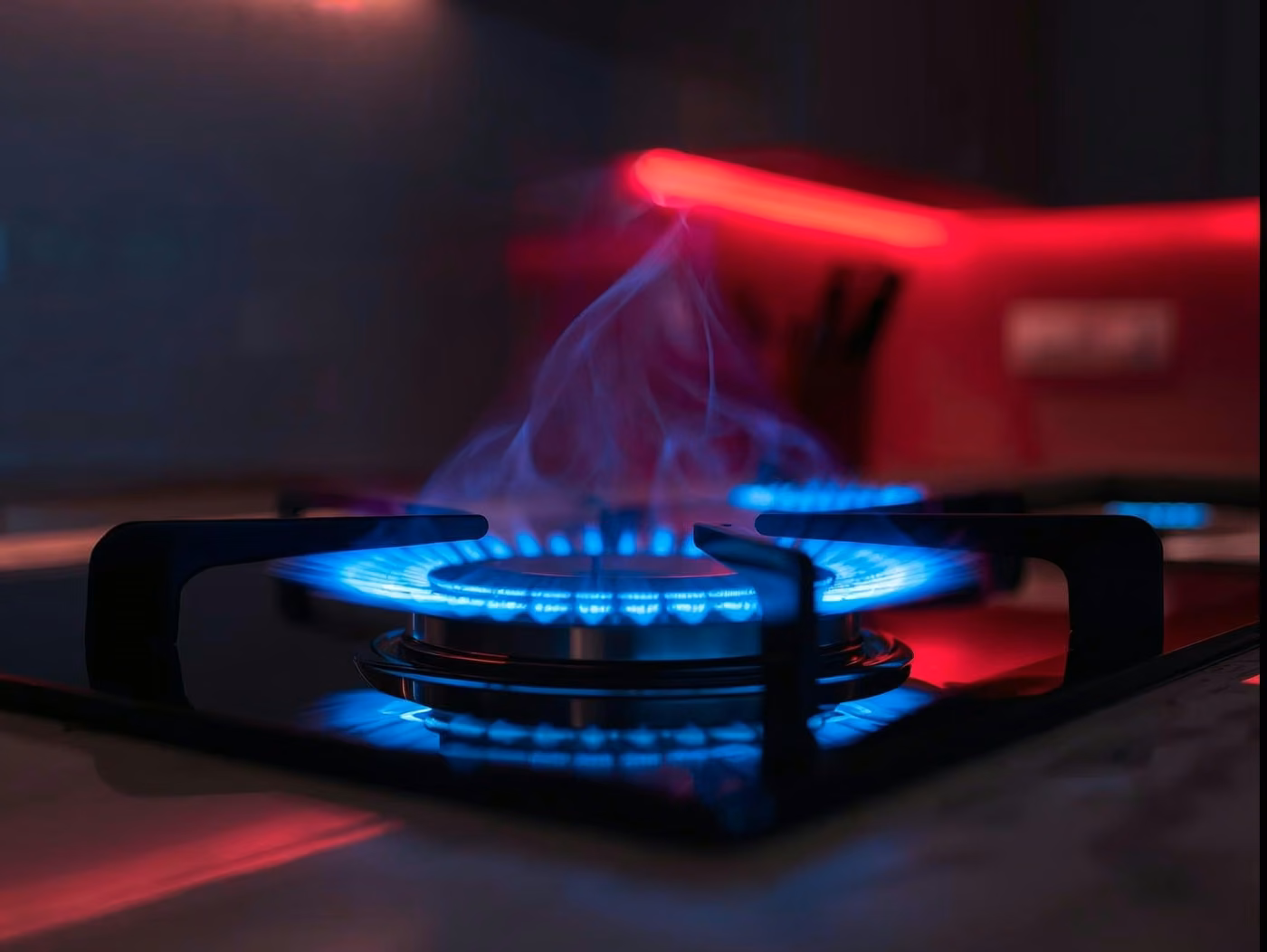 Close-up pan on gas hob with vivid blue flame, modern kitchen, subtle red_deep blue accents, no text, wide banner.